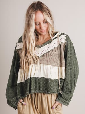 Woman wearing a layered outfit with a green patterned top and beige skirt on a plain background
