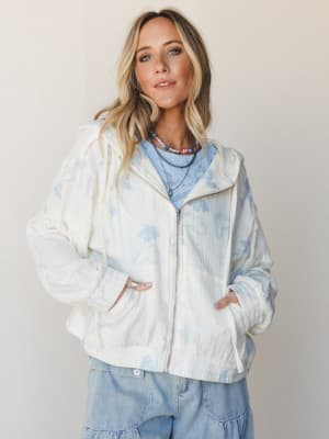 A relaxed, layered look built around a cream zip-up jacket with soft blue butterfly print — worn open over a powder blue knit top and tiered denim skirt, with layered beaded necklaces that pull the whole thing together.