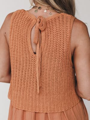 A close-up back view of a pumpkin-toned knit top with an open-back tie detail, layered over a gauzy skirt in the same warm terra cotta palette — the kind of effortless outfit that looks like it came together without trying.