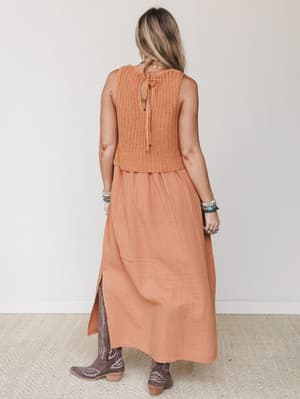 Shot from the back, this rust-toned maxi dress layers a chunky crochet knit bodice over a flowy gauze skirt — styled with cowboy boots and stacked turquoise bracelets for an effortlessly earthy, boho-Western feel.