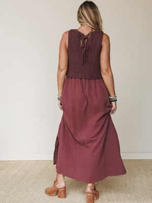 Shot from the back, this wine-toned maxi dress layers a chunky crochet knit bodice over a flowy gauze skirt — styled with stacked bracelets and suede clogs for a look that feels effortlessly collected.