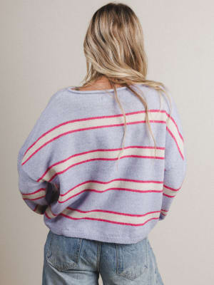 Back view of woman wearing a light purple sweater with red and white stripes on a plain background