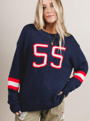 Woman wearing a navy sweater with red and white 'SS' design on a plain background