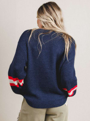 Person wearing a navy sweater with red and white accents on a plain background