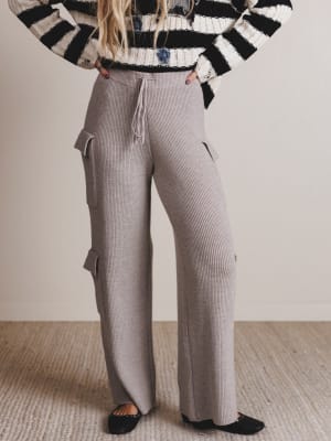 Person wearing a black and white striped sweater and gray ribbed pants on a neutral background