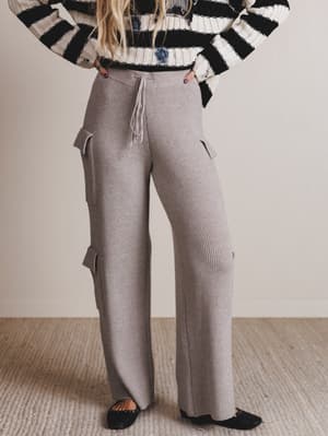 Person wearing a black and white striped sweater and gray ribbed pants on a neutral background