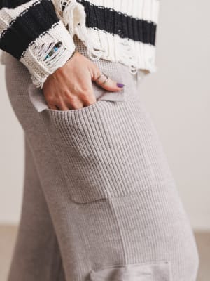 Person wearing a black and white striped sweater with gray pants, holding a phone in a pocket.