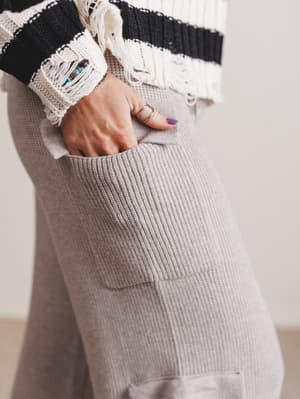 Person wearing a black and white striped sweater with gray pants, holding a phone in a pocket.