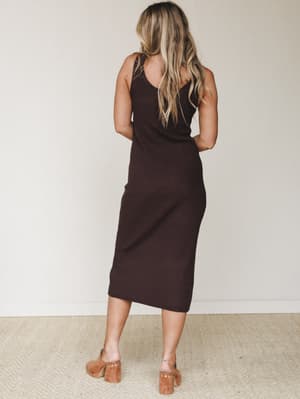 A ribbed dark chocolate midi dress shot from the back, fitted and sleeveless with a clean silhouette, paired with tan block-heel mules — the kind of dress that does the work so you don't have to.