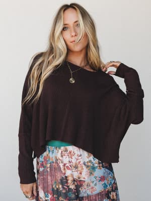 A relaxed, oversized ribbed crop sweater in deep plum-brown paired with a floral pleated midi skirt — the kind of mix that looks effortless but is absolutely intentional.
