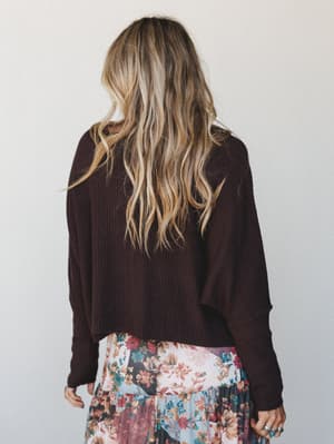 Shot from the back, a model in a deep plum-brown ribbed cropped sweater is paired with a colorful patchwork floral skirt — the kind of outfit that looks effortless but was definitely thought about.