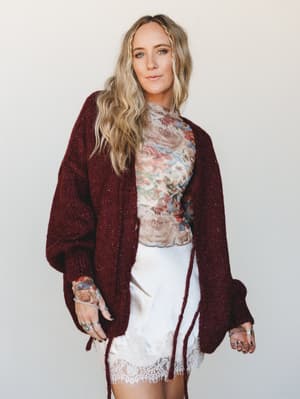 A layered, lived-in look built around an oversized burgundy knit cardigan worn open over a floral mesh top and a white lace-hem mini skirt — the kind of outfit that looks effortless but absolutely wasn't an accident.