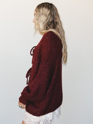 A side-profile shot of a chunky knit burgundy sweater with front tie detail, layered over a lace skirt — the kind of cozy-meets-romantic combination that makes fall dressing feel effortless.