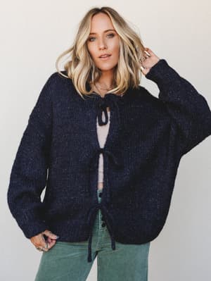 An oversized navy knit cardigan with tie-front closures worn open over a pale tank, paired with sage green wide-leg pants — the kind of cozy, collected outfit that looks effortless but was absolutely thought about.