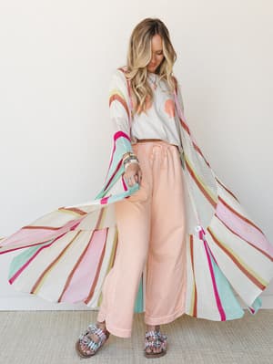 A breezy full-length striped knit kimono fans out mid-twirl over a seashell graphic crop tee and peach wide-leg pants — the kind of outfit that looks like it had a great summer.