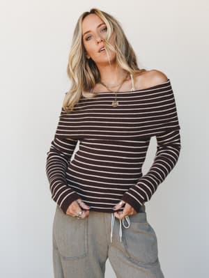 A relaxed off-shoulder striped knit top in deep chocolate and cream pairs with olive cargo-style pants — the kind of effortlessly put-together look that feels cozy enough for a coffee run but intentional enough for brunch with friends.