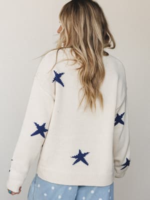 A back-view shot of a cream knit sweater with scattered navy star intarsia, styled with light blue polka dot pants — the kind of cozy, feel-good piece that makes a Tuesday feel intentional.