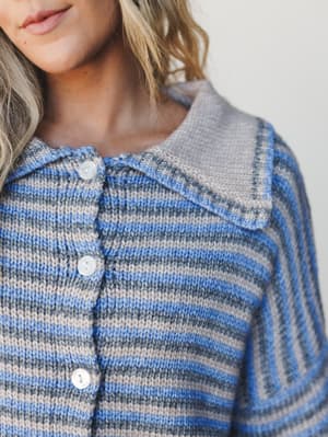 A close-up of a striped knit cardigan with a relaxed collar and pearl buttons — the kind of sweater that makes you want to pour something warm and stay a while.