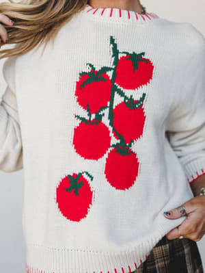 A cream knit sweater photographed from the back, featuring a bold intarsia tomato-on-the-vine graphic — the kind of piece that makes people stop you at the farmers market to ask where you got it.