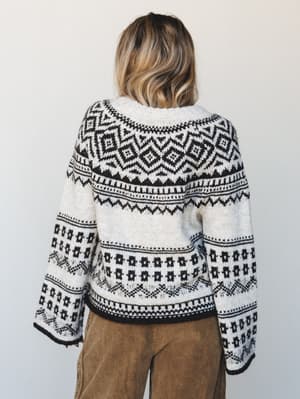 Shot from behind, a model wears a cream and black Fair Isle knit sweater with dramatic bell sleeves, paired with tan corduroy pants — the kind of sweater that makes a Saturday feel intentional.