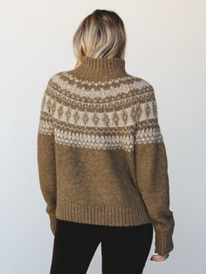 A cozy Fair Isle turtleneck sweater in heathered olive brown, shot from the back to showcase the detailed yoke patterning — the kind of sweater that makes you want to find a cabin and stay there.