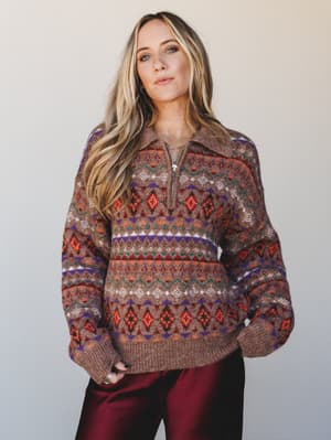 A cozy Fair Isle quarter-zip sweater in warm brown with pops of rust, purple, and teal, styled with deep burgundy satin pants — the kind of sweater that makes you want to stay out just a little longer.