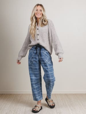 Woman wearing a gray sweater and blue plaid pants standing against a plain background