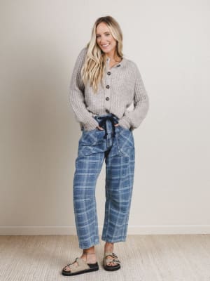Woman wearing a gray chunky sweater and blue plaid pants standing against a plain background