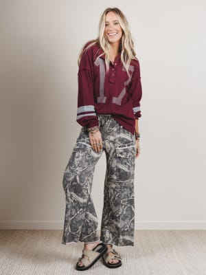 Woman wearing a maroon sweater with a number design and camouflage pants indoors.