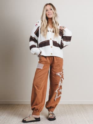 Woman wearing a patterned cardigan and brown pants against a plain background