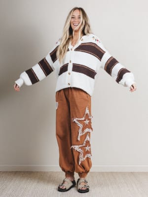 Woman wearing a striped sweater and brown pants with star designs against a plain background