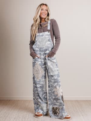 Woman wearing patterned overalls and a brown sweater against a plain background