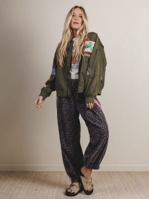 Woman wearing a green bomber jacket and patterned pants against a plain background