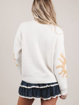 White sweater with yellow patterns worn by a person on a beige background