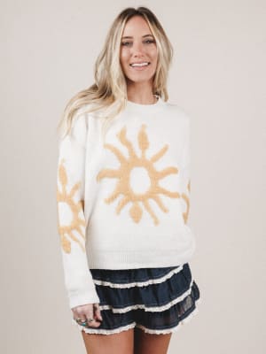 Woman wearing a white sweater with sun designs on a plain background
