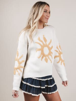 Woman wearing a white sweater with sun designs on a plain background