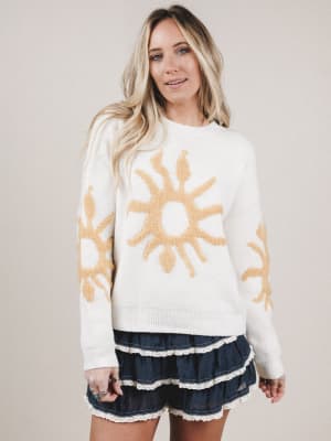 Woman wearing a white sweater with sun designs on a plain background