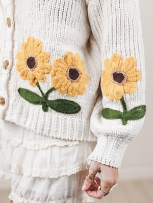 White sweater with yellow sunflower designs on the sleeves and chest.