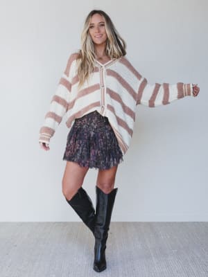 Woman wearing a striped sweater, floral skirt, and knee-high boots against a white background