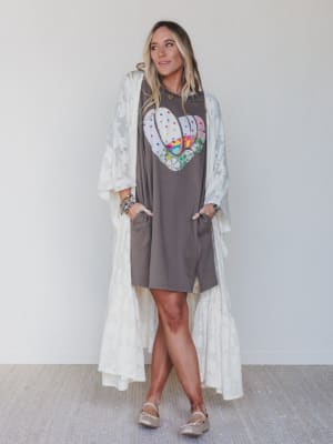 Woman wearing a gray dress with a colorful heart design and a white lace cover-up against a plain background.