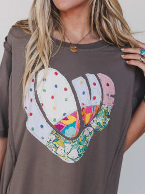 Person wearing a brown t-shirt with a colorful heart design.