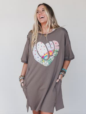 Woman wearing a brown dress with a colorful heart design on a plain background