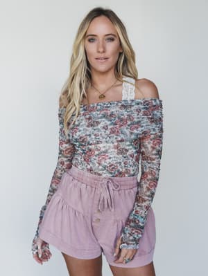 Woman wearing a floral off-shoulder top and pink shorts against a white background