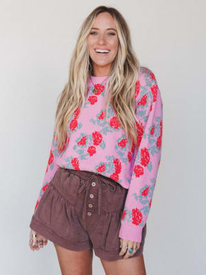 Woman wearing a pink floral sweater and brown shorts against a white background