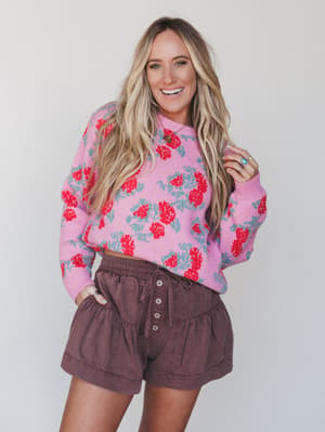 Woman wearing a pink floral sweater and brown shorts against a white background