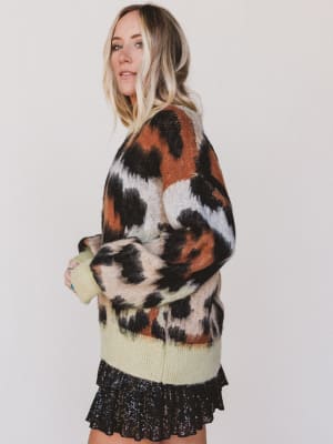 Woman wearing a patterned sweater over a light green top with a black skirt on a white background