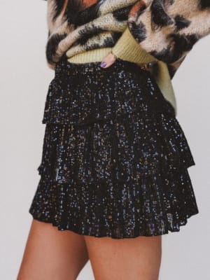 Black sequin skirt worn with a patterned sweater on a plain background