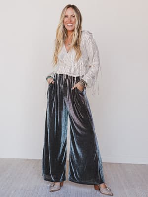 Woman wearing a white blouse with fringe and black velvet wide-leg pants against a white background
