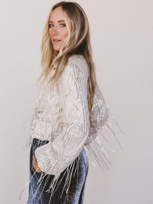 Woman wearing a white fringe jacket against a plain background
