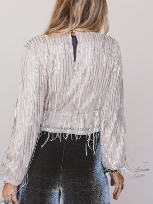 Person wearing a silver sequin jacket with fringe on a plain background